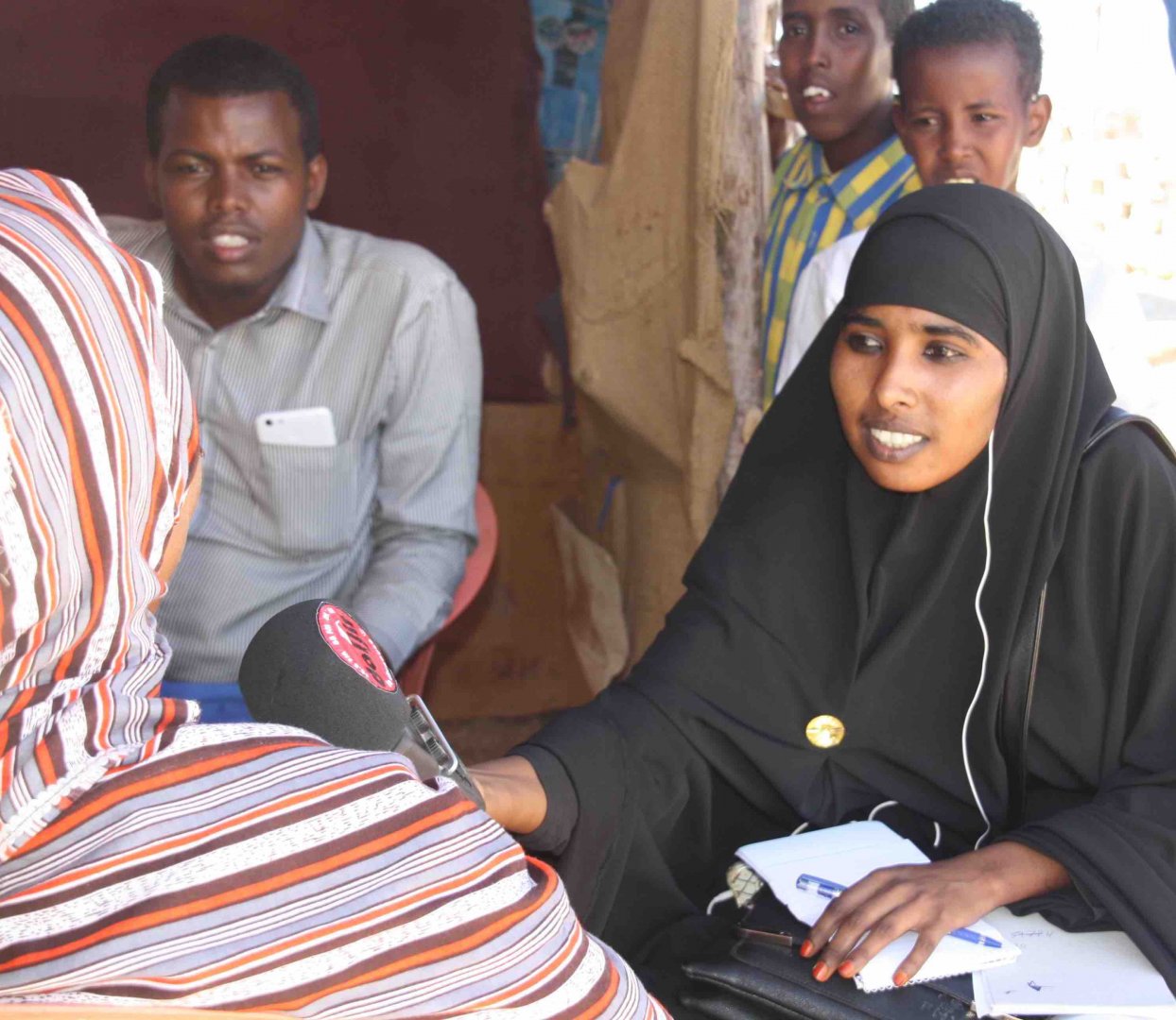 A Somali woman dressed in black holds a recorder up to another woman.
