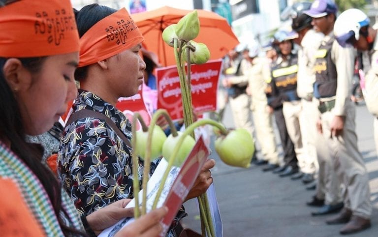Women hold lotus flowers as authorities look on outside Olympic Stadium in Phnom Penh on March 8, 2019, during a rally marking International Women’s Day (Licadho)