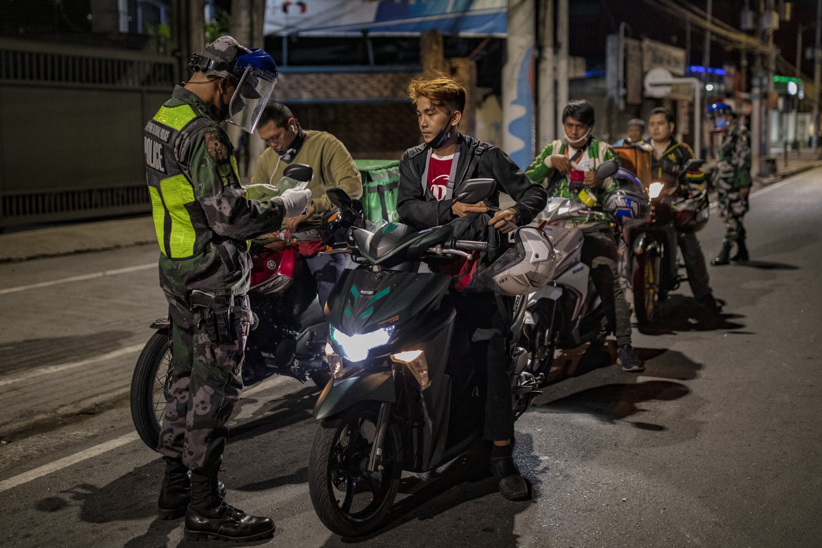 Policeman stops a line of people on motorcycles at a checkpoint in the Philippines