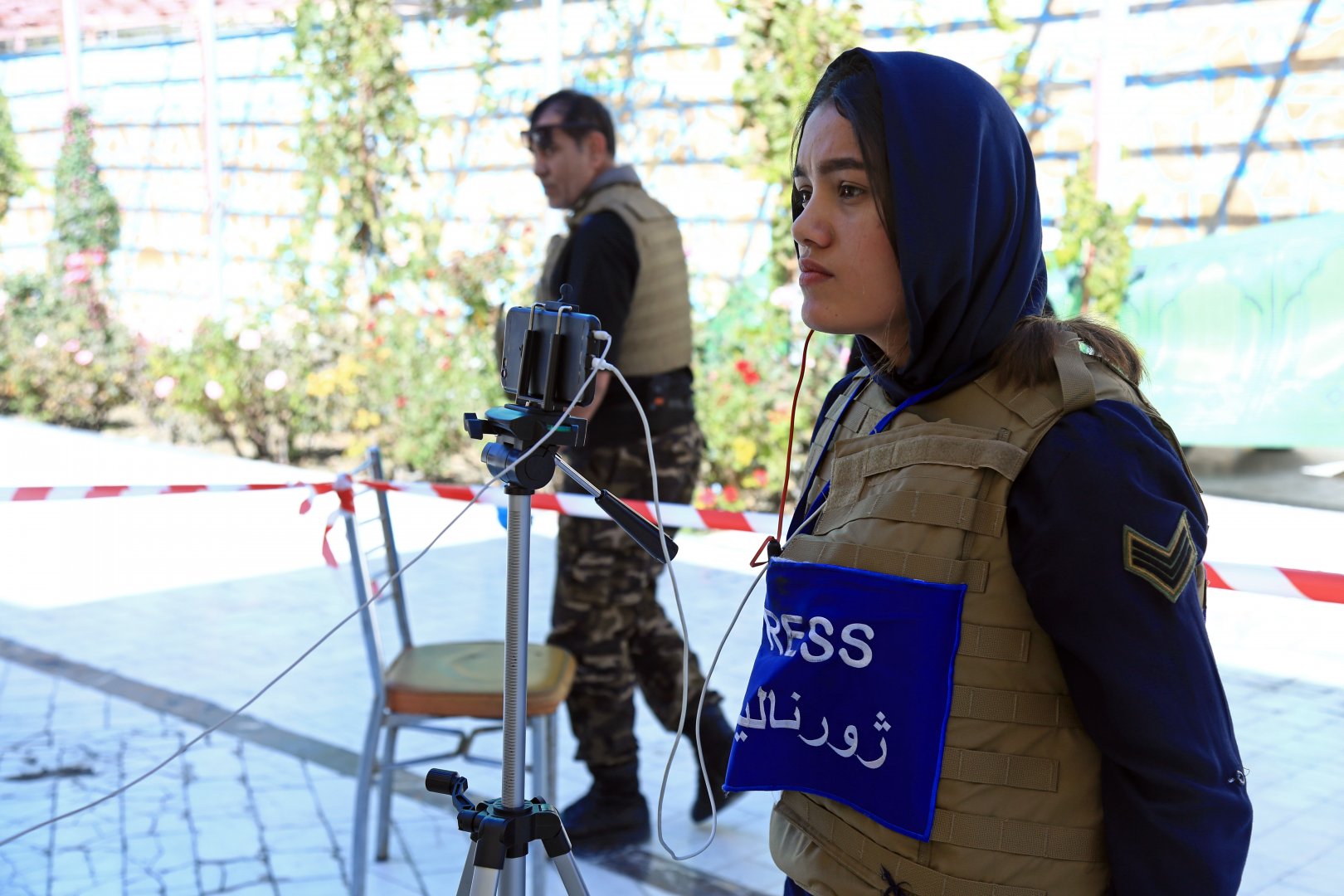 Journalist wearing a press vest and filming on her phone