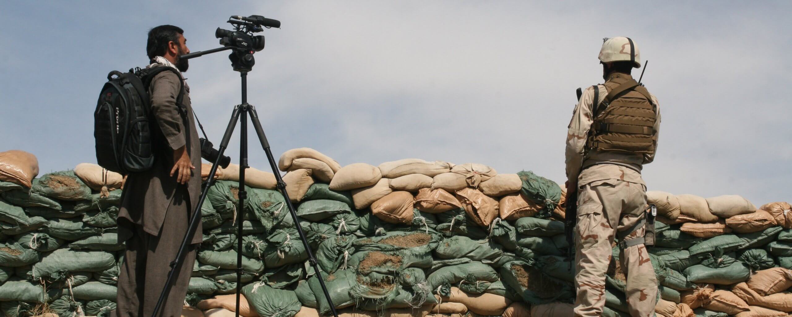 A journalist stands on a watch point with a camera and a solidier in Afghanistan