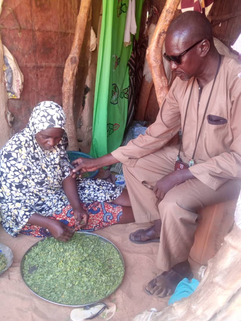 A man is interviewing a woman for radio while she is preparing food