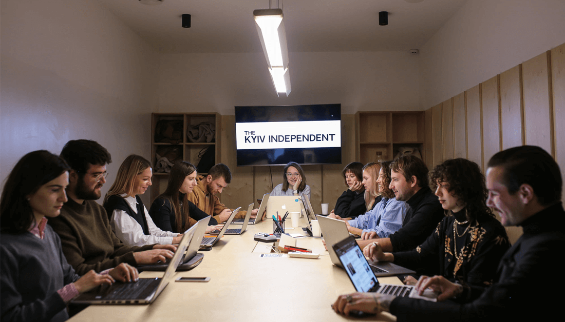 Conference table with men and women with laptops sitting around it. A woman sits at the head of the table, under a banner that reads The Kyiv Independent