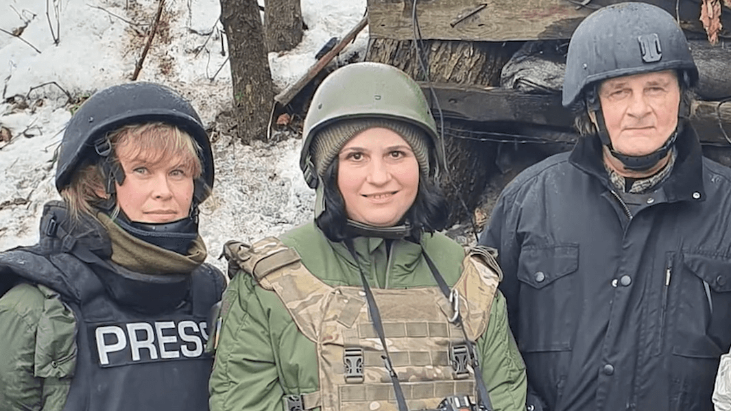 three journalists stand in a row wearing flak jackets and helmets. Two are women and one is a man.