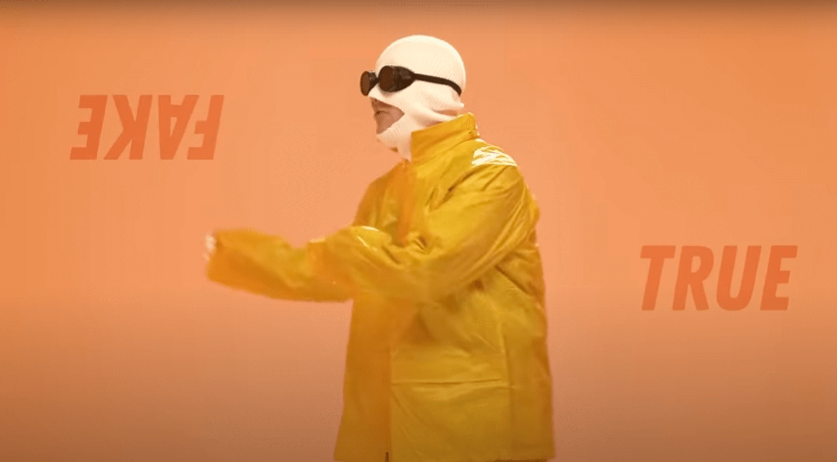 a person wearing a white balaclava, sunglasses and a yellow jumpsuit against an orange background with the words true and fake on either side of them