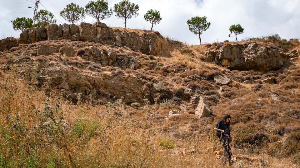 Rianna Tassabehji makes her way amid rocky outcrops on a trail that twists at the bottom of a hill. Batloun, Lebanon. September 14, 2022. (Chris Trinh/The Public Source)
