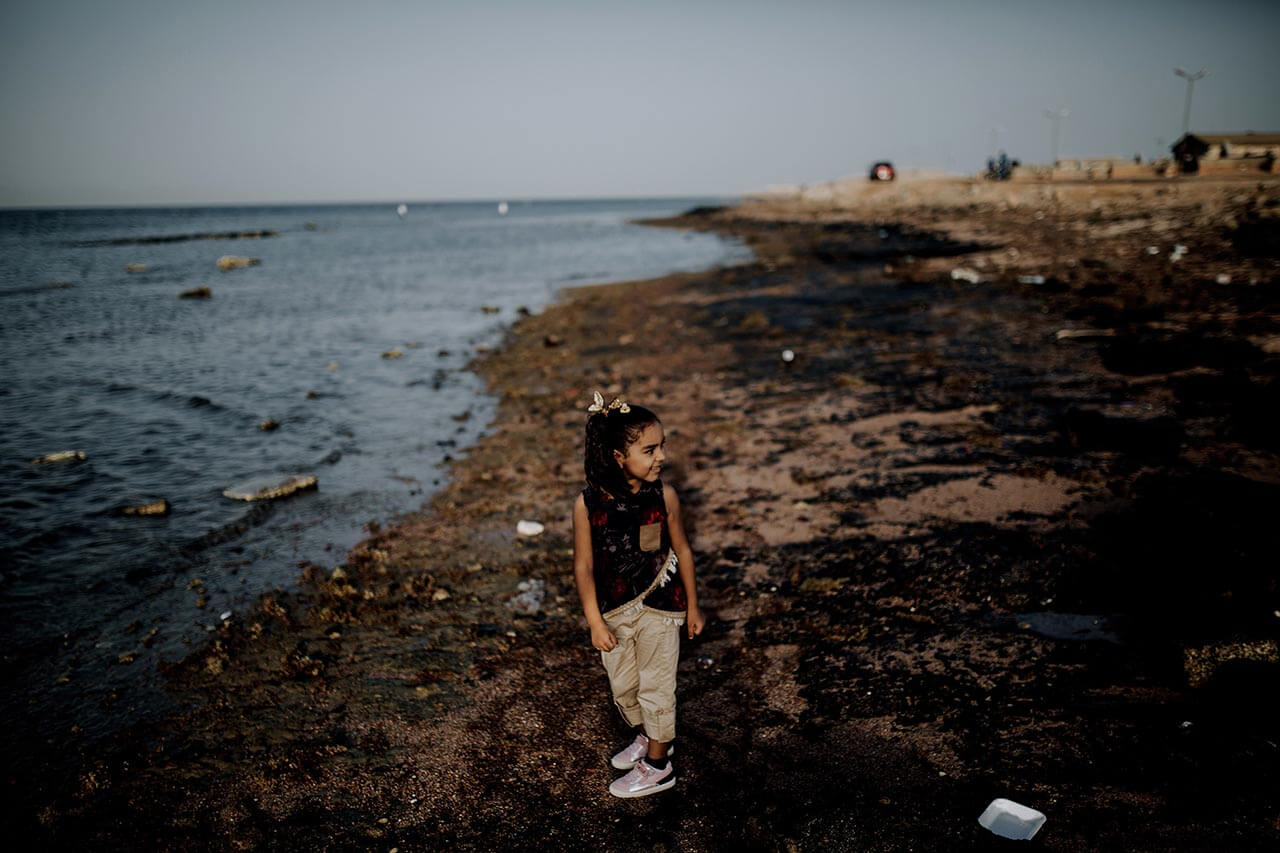 A young girl stands on the beach of Ras Ghareb where oil spills have turned the sand black.